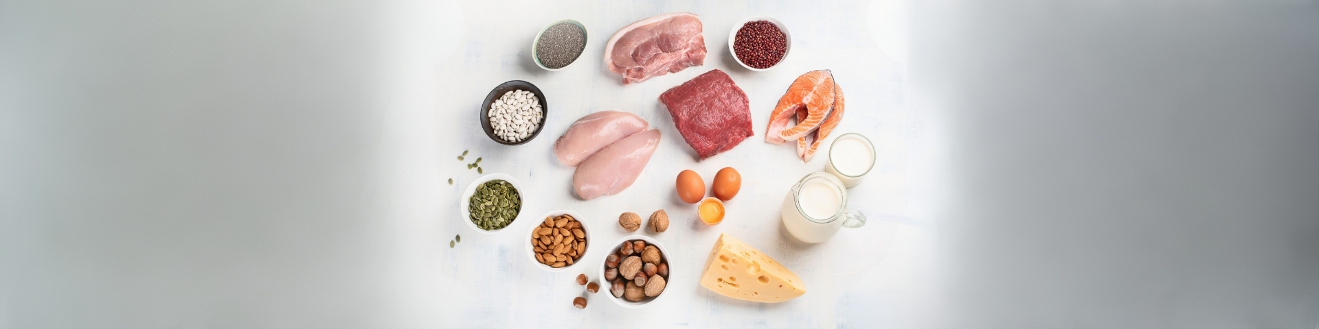 Aliments riche en protéines sur fond bland : poulet, oeuf, saumon, produits laitiers, céréales, légumineuses... Image utilisées pour illustrer un article de blog de 1Defy Nutrition Sportive made in France, pour parler des bienfaits des réigmes riches en protéines